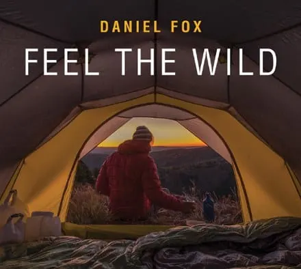 Feel the Wild book cover with a shot from inside a camping tent with a person outside drinking on a sunset