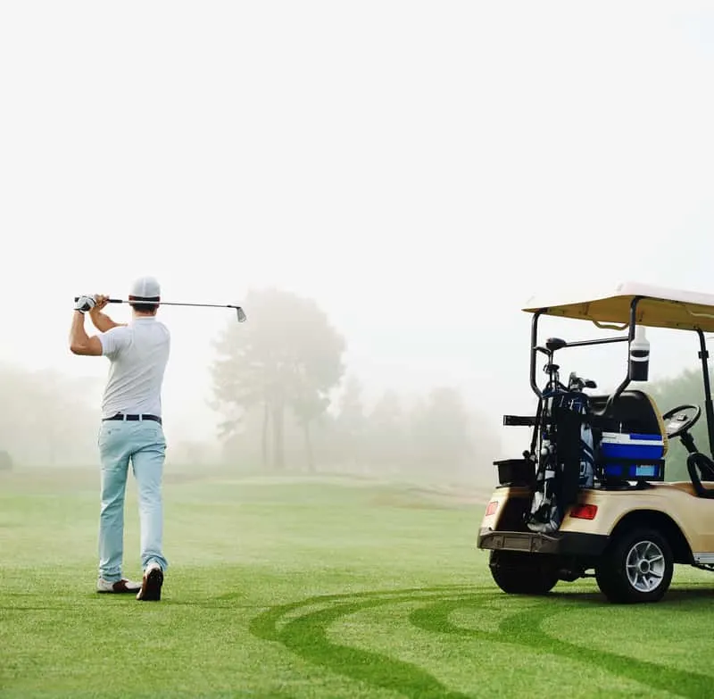 golfer in fairway with cart playing shot towards green,