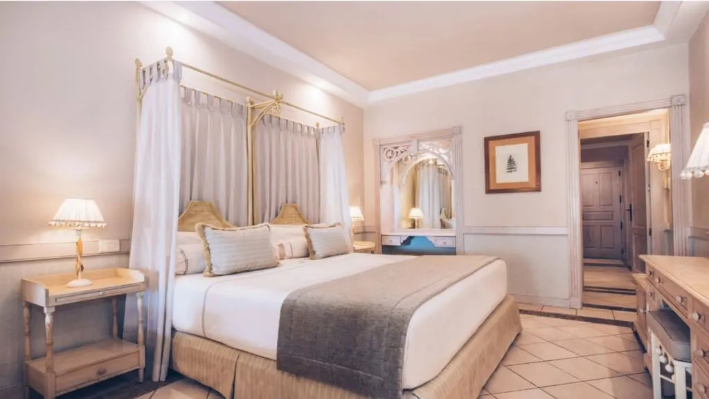 These all inclusive adults only tenerife hotels will take your breath away, interior of lavish hotel room with large king size bed and desk area with small bedside tables with lamps on and a view down the corridor to the door