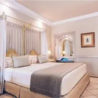 These all inclusive adults only tenerife hotels will take your breath away, interior of lavish hotel room with large king size bed and desk area with small bedside tables with lamps on and a view down the corridor to the door