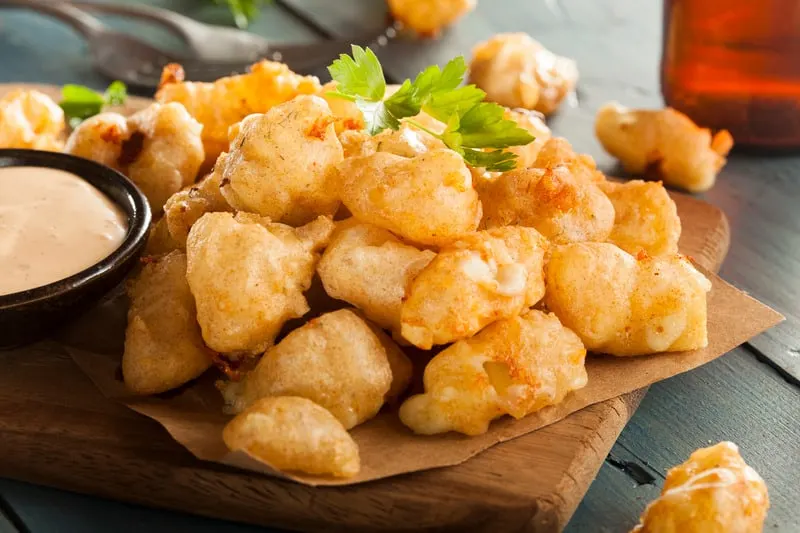 Beer Battered Wisconsin Cheese Curds with Dipping Sauce on a paper on top of a wooden tray