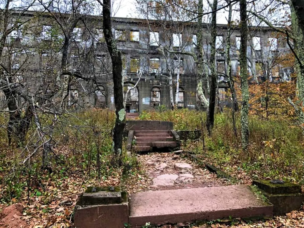 See the abandoned places america has to offer, broken steps leading through an overgrown garden to a large concrete ruin with many empty windows and an arched entrance