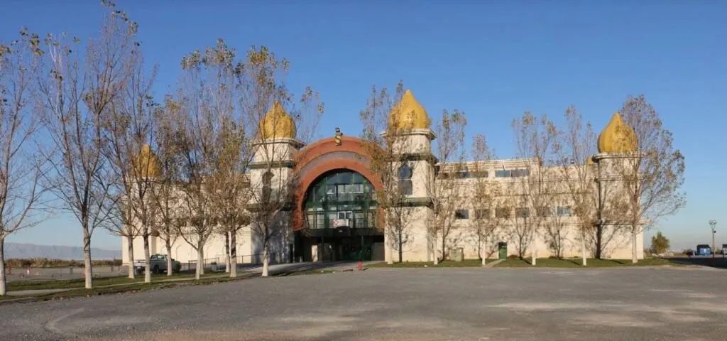 Find some abandoned places in america, large building with tall golden pointed turrets surrounded by tall bare trees under an open blue sky
