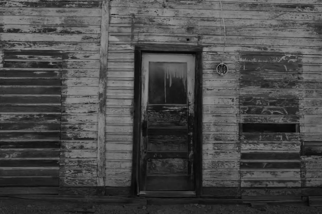 Hold your nerve in the creepiest abandoned places in America, foreboding doorway set in a black and white wooden house with boarded up windows