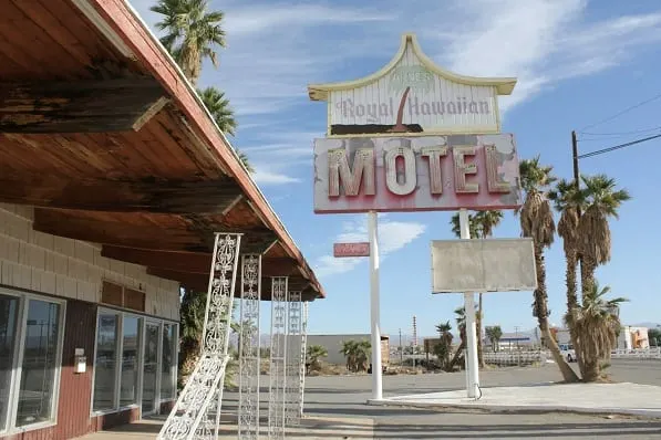 Discover some of the best abandoned tourist attractions, front of abandoned motel with large faded sign saying "Royal Hawaiian MOTEL" in pink and white lettering next to a dilapidated covered porch