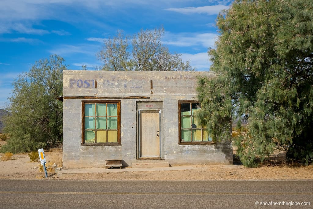 Travel to the best abandoned buildings in America, small single storey grey building with covered broken windows and faded lettering