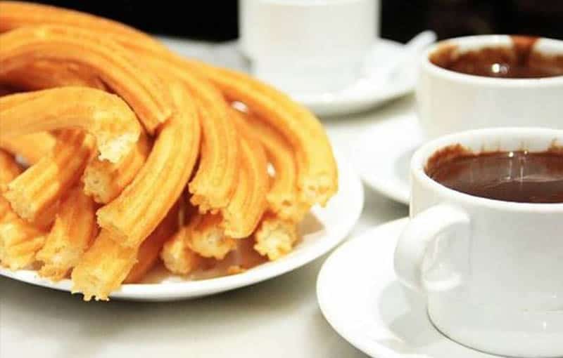 Churros dish from Madrid sitting next to ceramic cups of melted chocolate