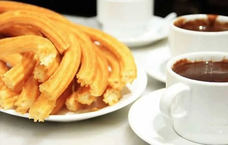 Explore the wonders of Spain food culture, Churros dish from Madrid sitting next to ceramic cups of melted chocolate