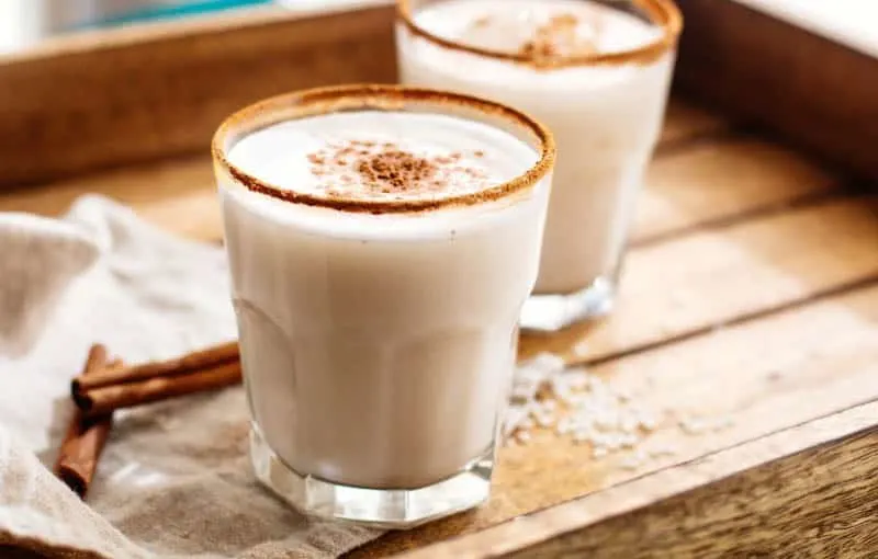 Enjoy some popular food in Spain, Horchata Drink in small tumbler glasses sitting on a wooden tray with some cinnamon sticks nearby