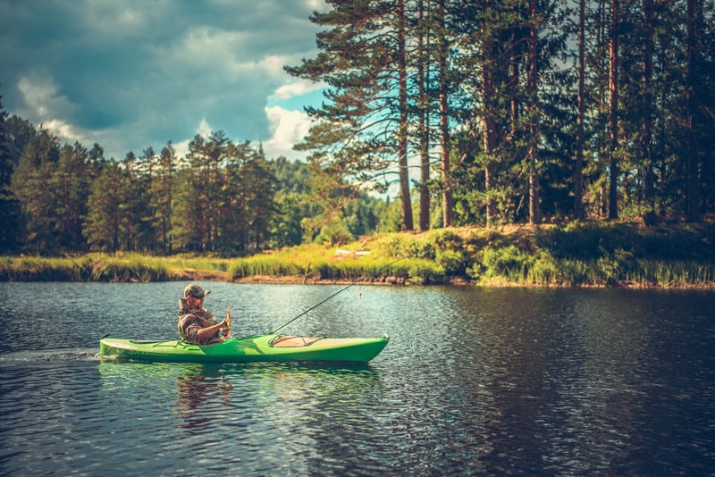 Kaukázusi férfi a 30-as éveiben, aki kajakból horgászik. Lake Recreation Time. legjobb felfújható kajakok horgászathoz