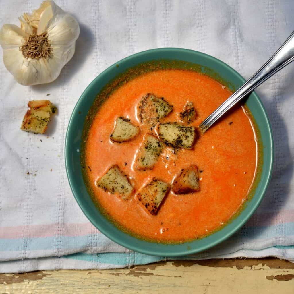 a red soup on a green bowl with garlic croutons on a table