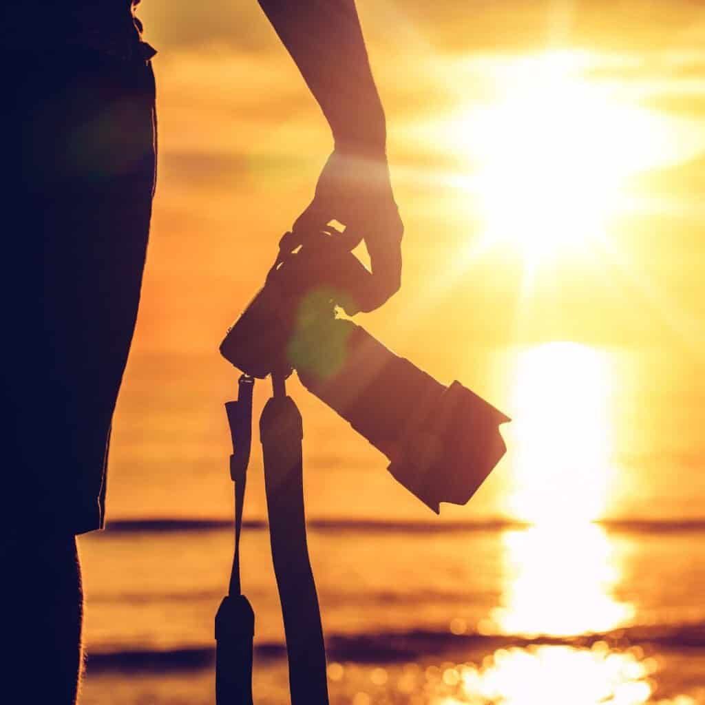 a photographer carrying a camera on a beach during a sunset