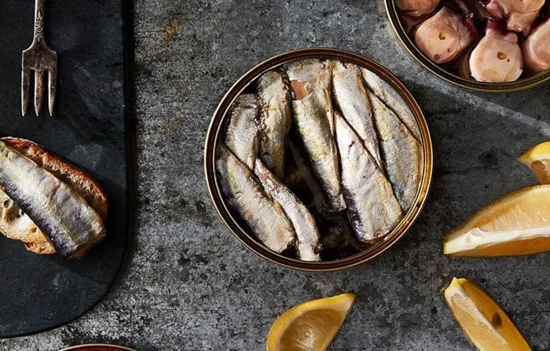 overhead shot of Tinned Seafood dish with fruits on the side and a fish and a fork on a plate