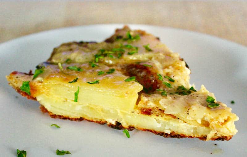 close up of 1/8 of a round Tortilla Española, Spanish Omelet dish with several garnishes on top