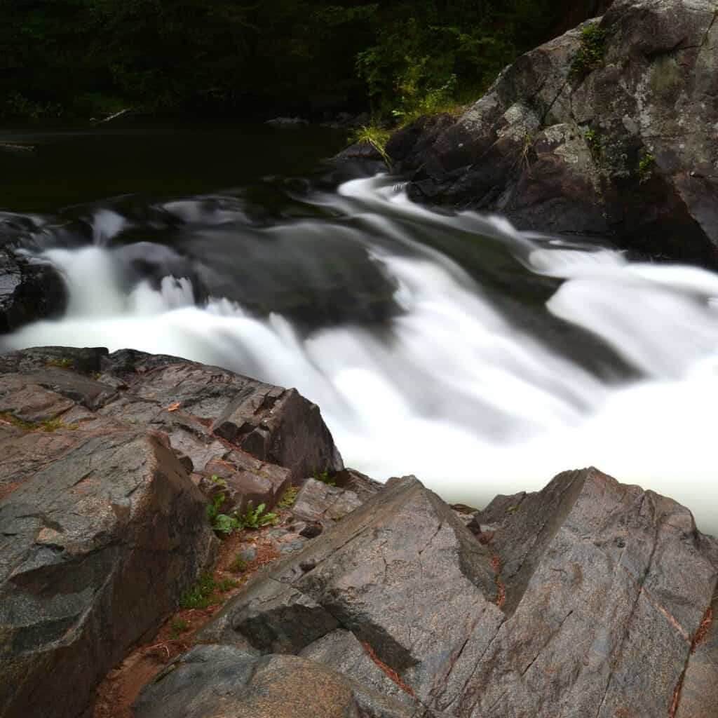 water flowing over rocks in the middle of a river with wet rocks in front