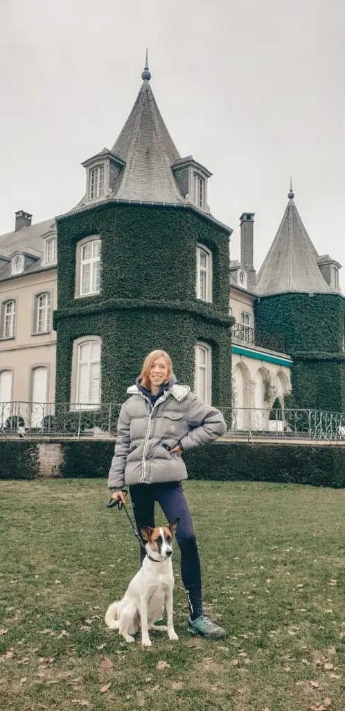 a woman with a dog standing with a building with green and white 
chateau la hulpe brussels, solvay castle