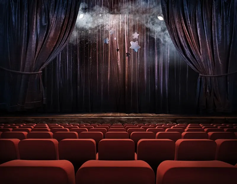 inside of an empty magic theatre with red chairs and velvet curtains and stars hanging from ceiling