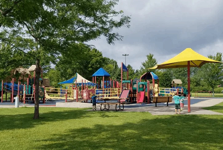 Romantic things to do in appleton, Wisconsin, Appleton Memorial Park with colorful playground containing walkways and slides surrounded by green grass and trees on a grey cloudy day