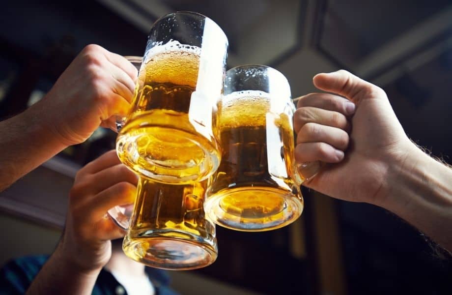 Try out all these amazing Wisconsin beer brands, close up shot of three hands each holding a tall glass tankard filled with golden fizzy beer together in celebration