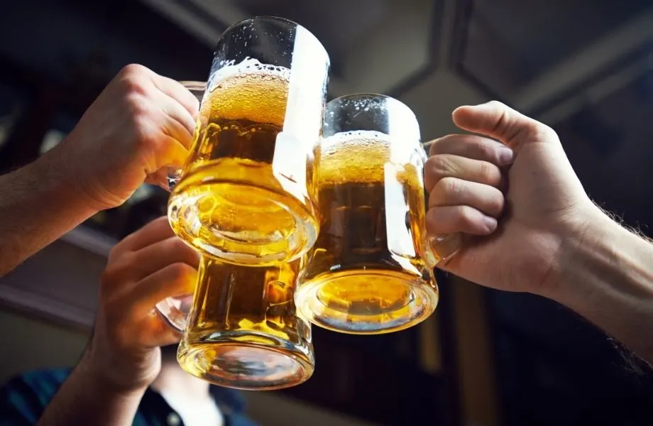 Try out all these amazing Wisconsin beer brands, close up shot of three hands each holding a tall glass tankard filled with golden fizzy beer together in celebration