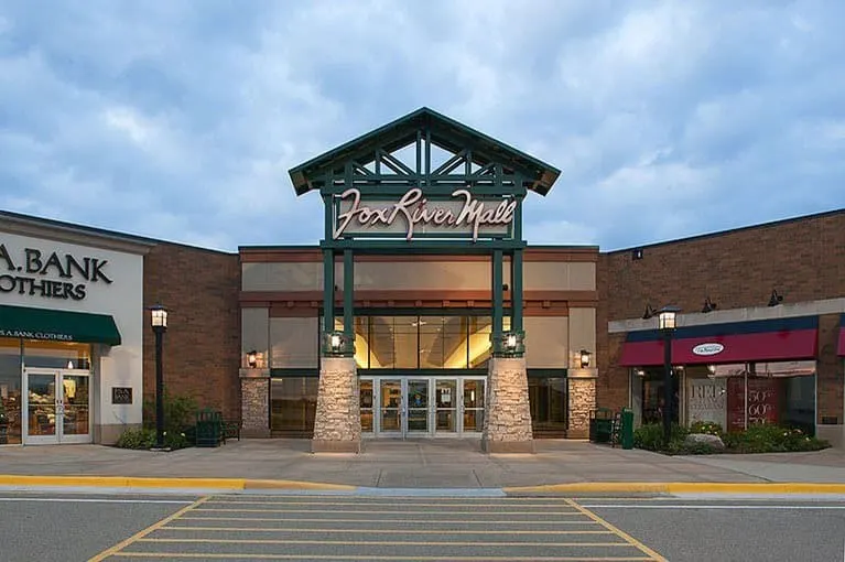 Best place to visit in appleton wisconsin, Front view of Fox River Mall with large green sign mounted on stone pillars under a cloudy sky at dusk