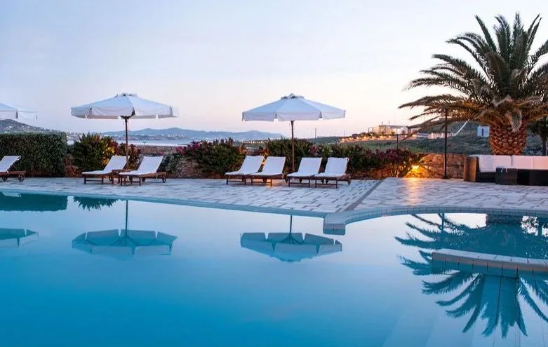 pool with umbrellas, beach chairs, and palm tree with a view of the town sea, and sky