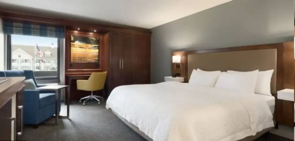 Don't miss all the things to see in appleton wi, interior of hotel room at the hampton inn appleton with large white bed next to wardrobe and small work desk with larger armchair to one side