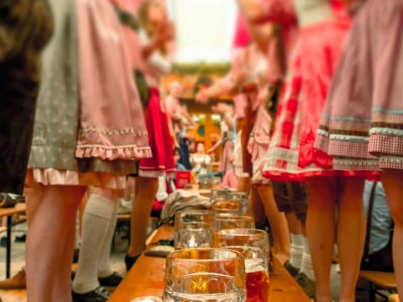 enjoy Oktoberfest in Milwaukee, people dressed in Bavarian dress standing over table of beers