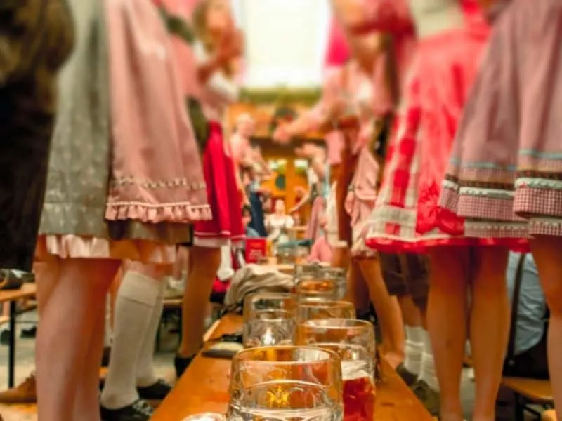 Enjoy these Milwaukee things to do in October, close up view of people decked out in party dresses standing next to a low table covered in lines of beer glasses