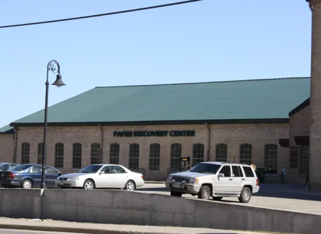 Discover what to do in appleton WI, view of Paper Recovery Centre building with long green tiled roof and parking lot with several cars in front on a bright day