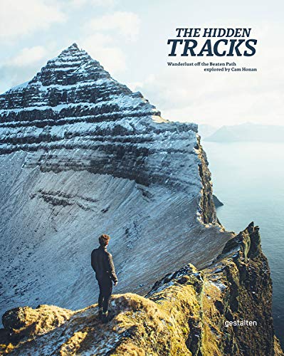 Destination coffee table books, book cover showing person standing on thin rocky ledge looking out at the peak of a mountain which itself is overlooking the sea with misty island in the distance