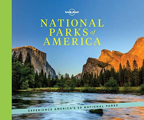 Coffee table travel books, book cover showing lake in national park with trees surrounding the shoreline and large stone mountains in the distance under a blue sky