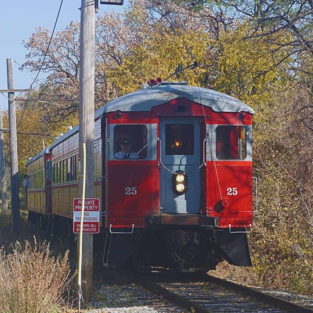 a red and white train traveling down the tracks with trees around