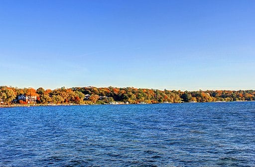 calm waters of the lake in the foreground and a rolling collection of trees in fall colors on the opposite bank