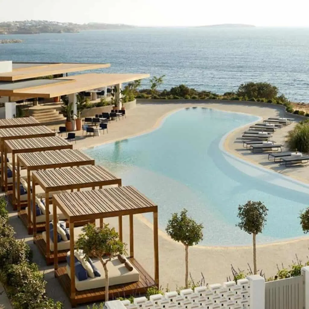 an aerial view of the pool and beach area at a luxury resort with beds and canopy, trees, and pool chairs, Luxury Accommodation In Paros