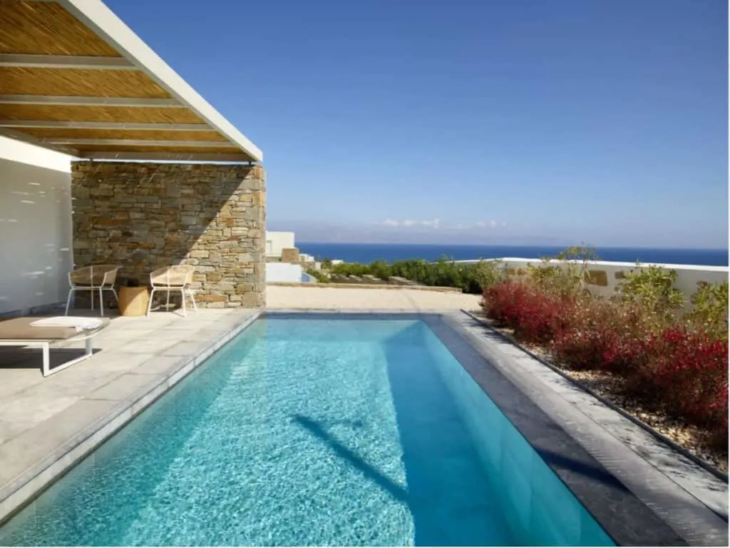 a small pool with a beach chair and bushes with a view of the sea and blue sky