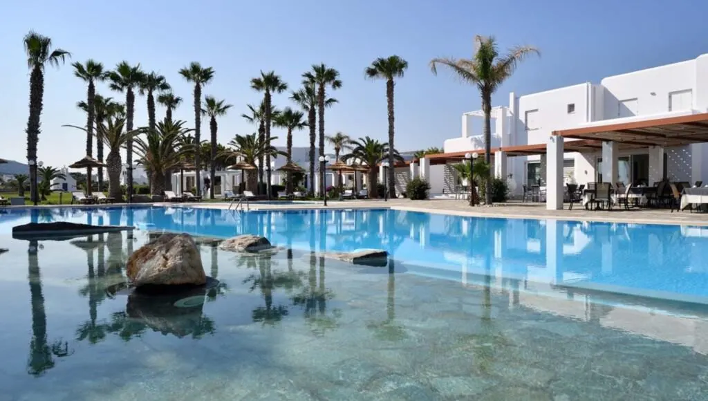 view of the pool at Astir of Paros with reflection of palm trees on the water and a white building on the side