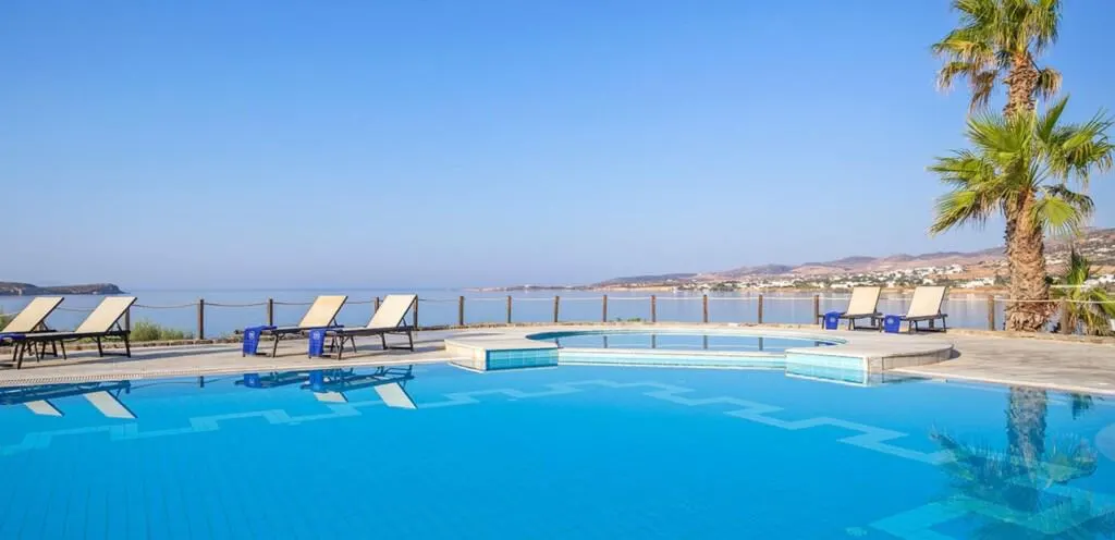 pool view at hotel poseidon with beach chairs, palm trees, the view of the town, sea, and sky