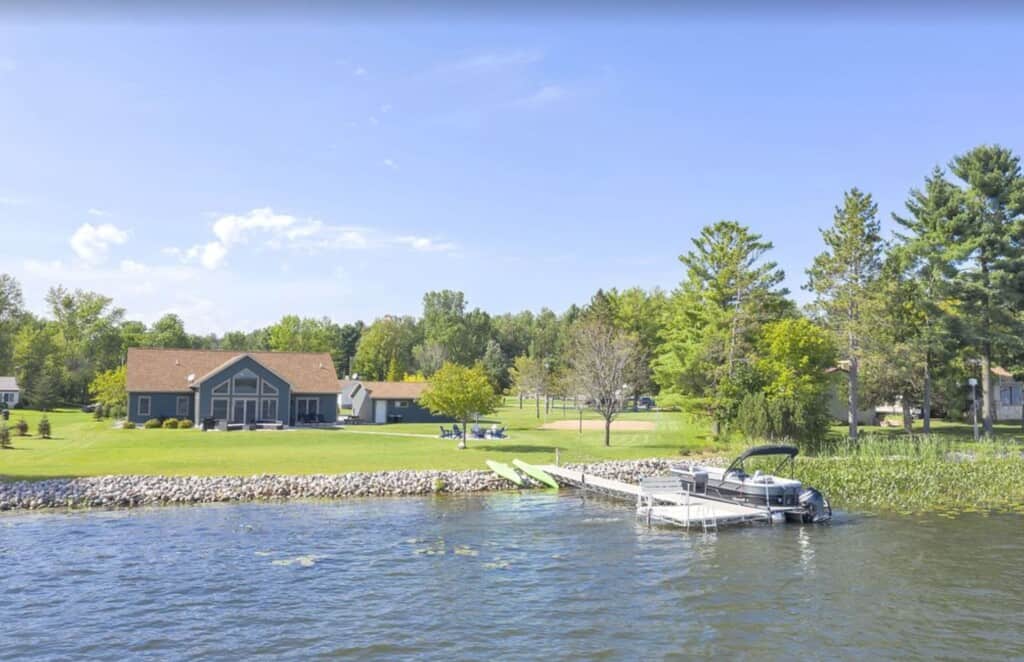 Treat yourself to wisconsin cabin resorts, view of cabin from lake with wooden jetty and boat moored alongside green lawns and tall trees on a bright day