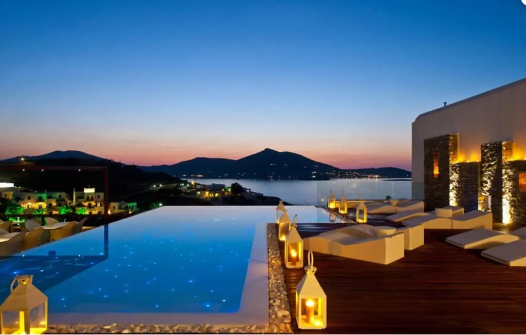 a view of Senia Hotel pool surrounded by lamps and pool beaches with the view of the sea and mountains at night