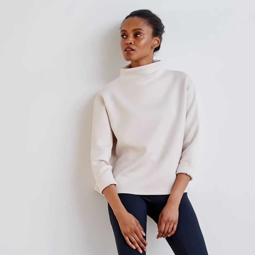 top recycled clothes company, black woman wearing a white turtleneck with loose fit and dark navy leggings