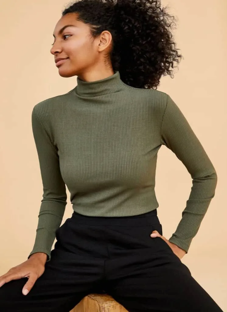 zero waste clothing company, black woman wearing green turtleneck and black pants looking off to the side