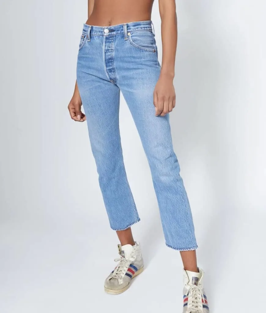 best Recycled Clothing Brands for jeans, image of dark-skinned person from mid-chest down wearing light blue ankle crop jeans and well-loved hightop shoes