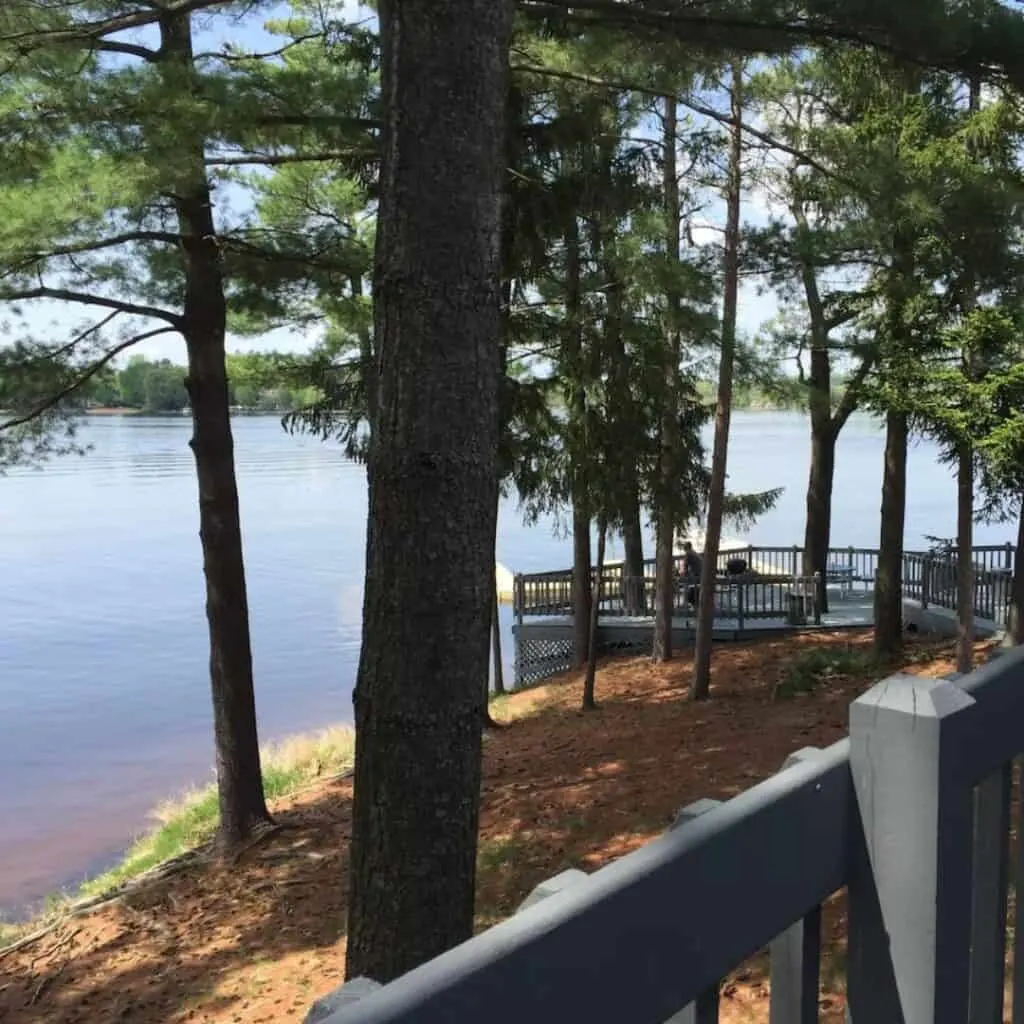 a view of a lake, trees, and a deck from a cabin near Lake Delton