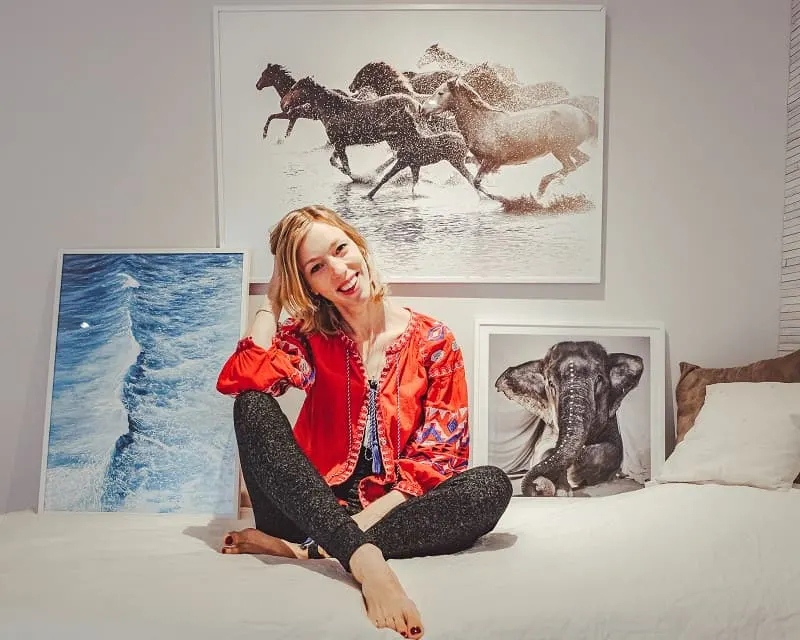 a woman on top of a bed surrounded by paintings of horses running, waves, and an elephant