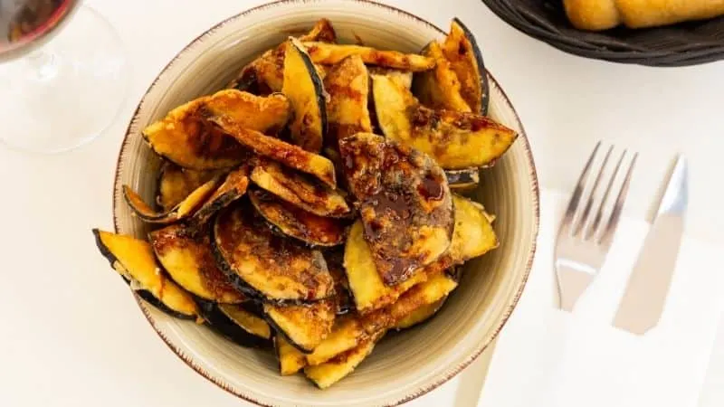 Spanish christmas food, Berenjenas con Miel food, crispy looking eggplant chops on a bowl with fork and knife