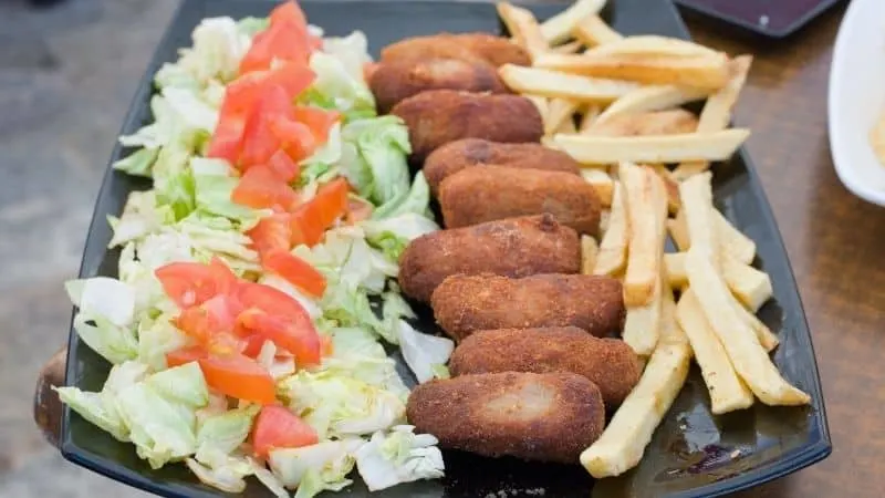 Traditional Spanish christmas food, Cured Ham Croquettes, cabbage and tomato, fried ham, french fries on a black plate