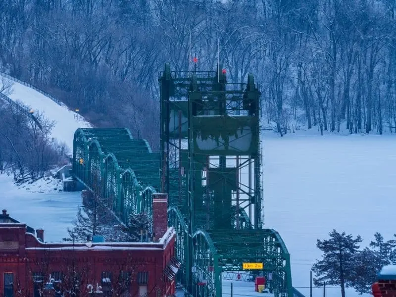 best wisconsin christmas towns, snow covered bridge over frozen, snow-covered lake surrounded by snowy forest