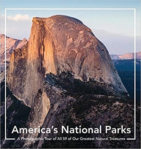 beautiful gifts for national park lovers, cover of coffee table book reading 'America's National Parks: A Photographic Tour of all 59 of Greatest Natural Treasures' with photo of stony mountain at dusk