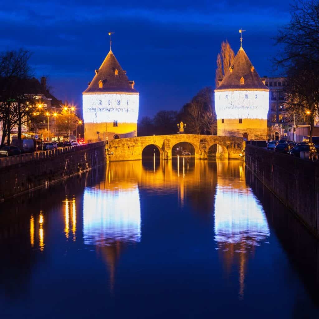 a bridge over a canal with two toes at night with lights on it reflecting over a canal